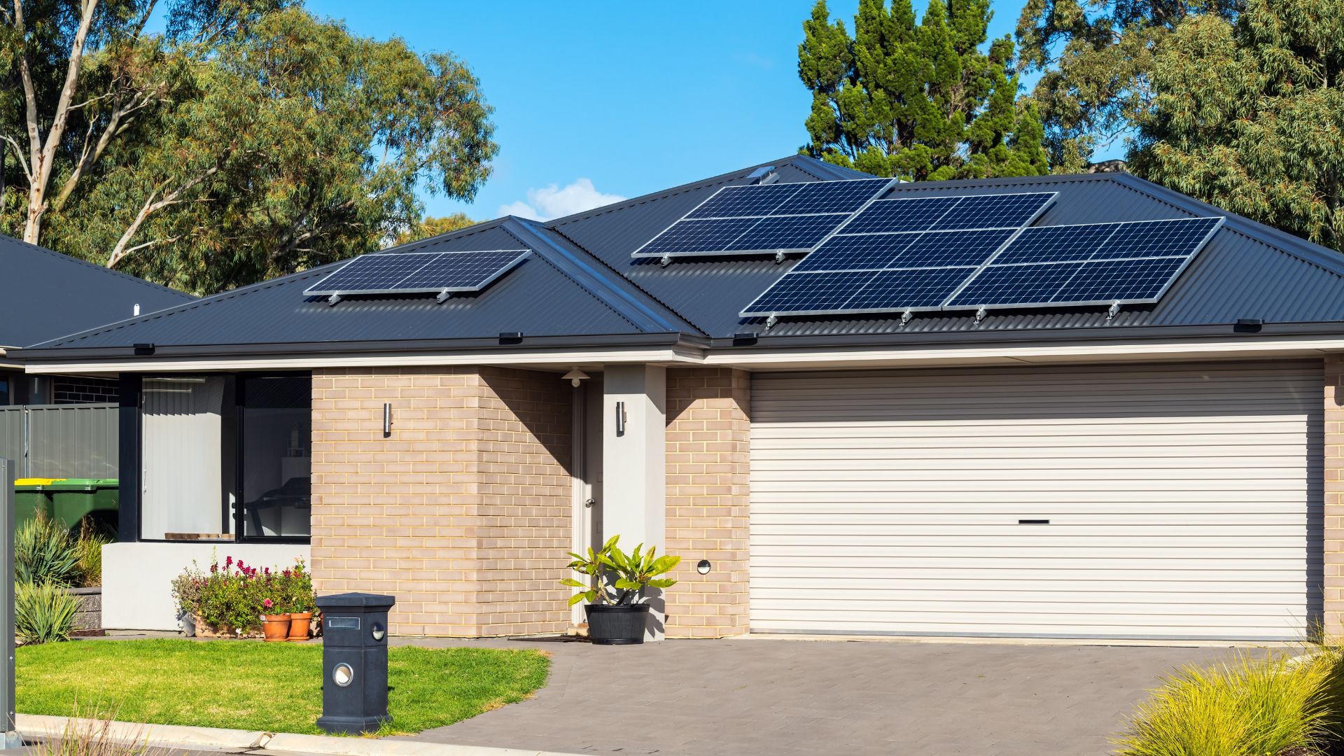 Modern suburban house with solar panels on dark roof, landscaped front yard