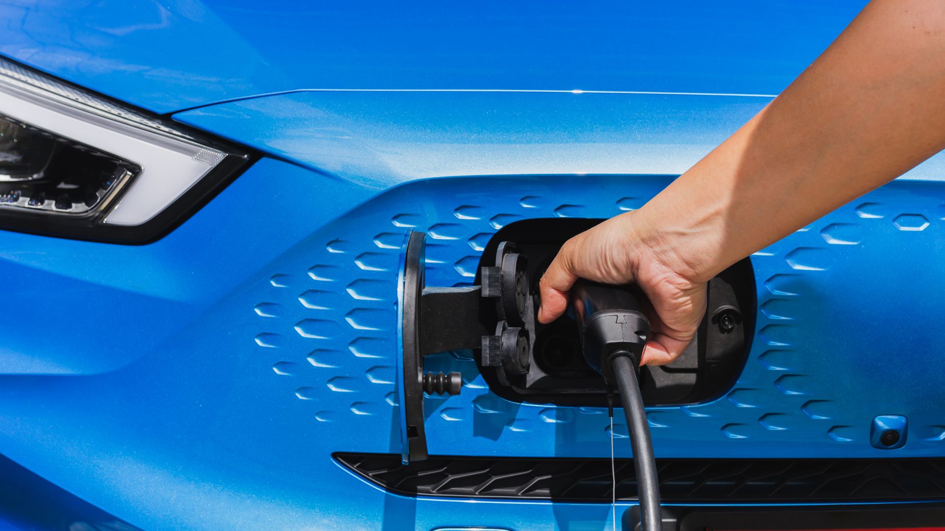 Hand plugging charging cable into electric vehicle charging port