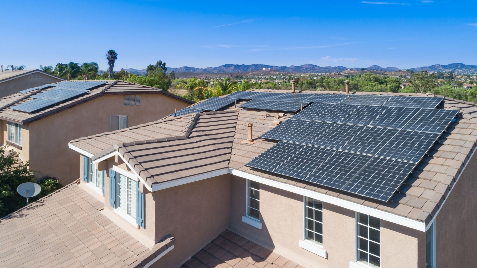 Residential house with large solar panel installation on roof, mountain backdrop