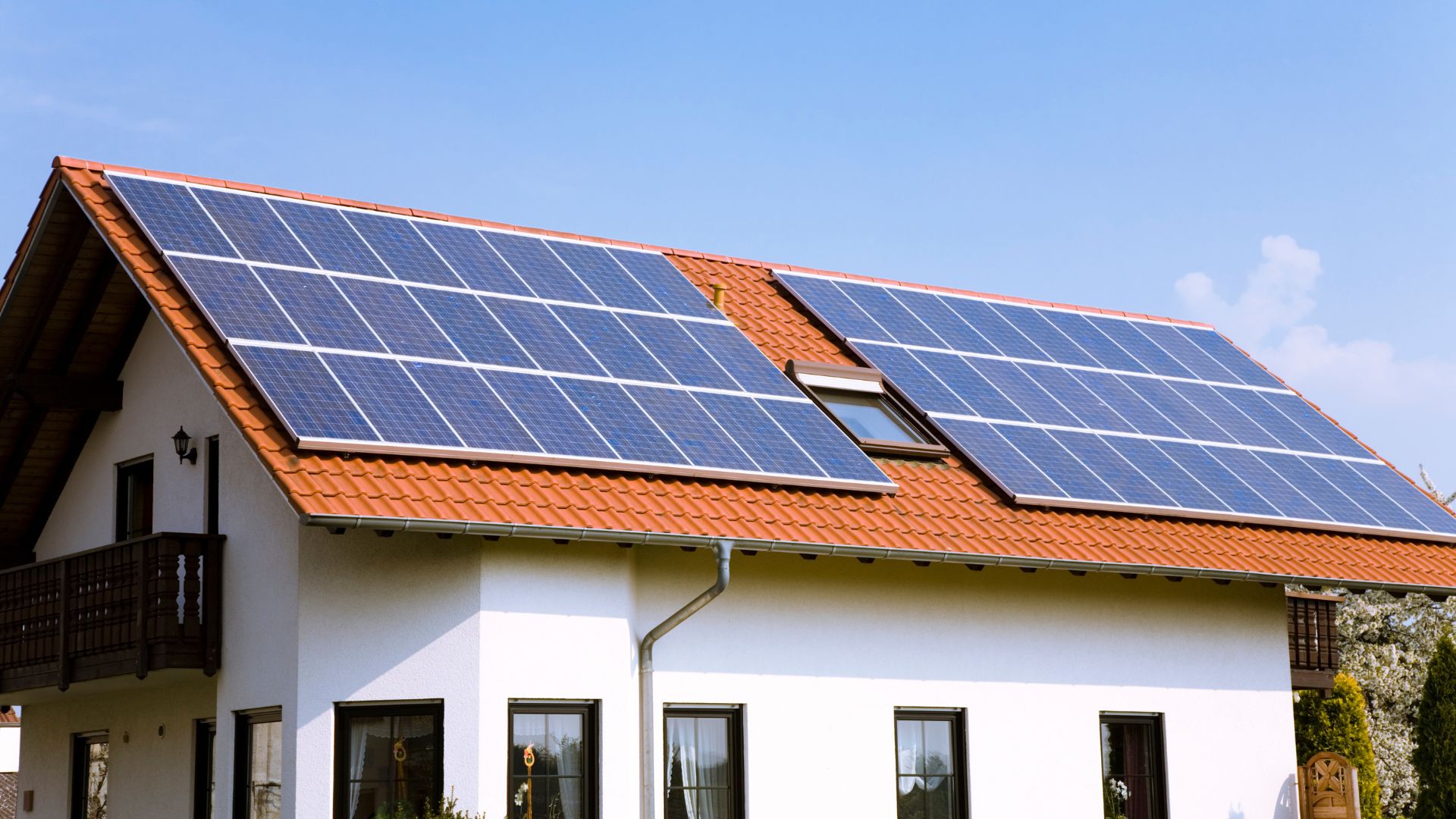 White house with multiple solar panels on orange tiled roof against blue sky